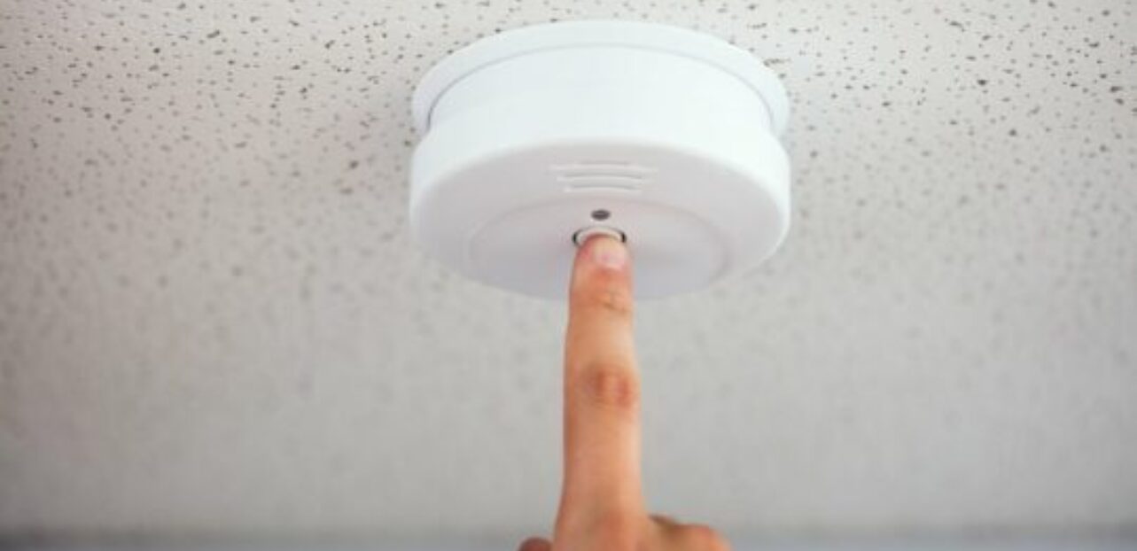 En finger trykke på en røykvarsel festet på takhimmel. Foto.
